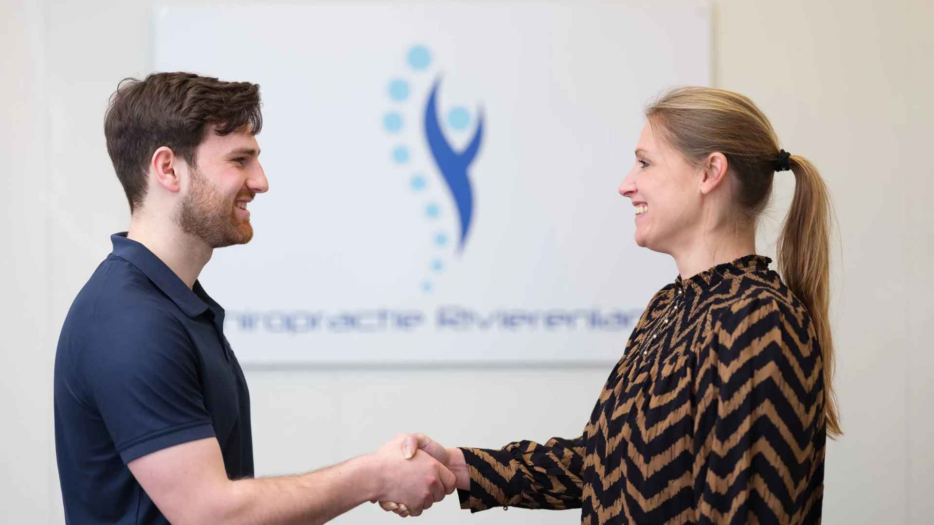 Chiropractor in gesprek met patient bij Waterland Chiropractie Culemborg met wervelkolommodel en Chiropractie Rivierenland logo